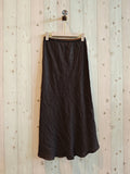Black skirt hanging on a wooden hanger against a light wooden panel background