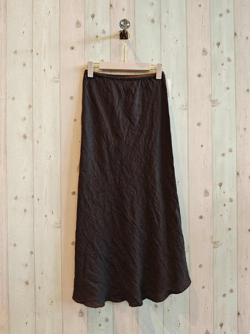 Black skirt hanging on a wooden hanger against a light wooden panel background