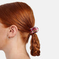 Person with red hair in a braid wearing a colorful scrunchie on a white background