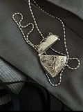 Silver necklace with intricate designs on a dark fabric background