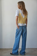 Person wearing a yellow top with floral patterns and blue jeans against a plain wall.