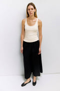 Woman wearing a white tank top and black pants against a white background