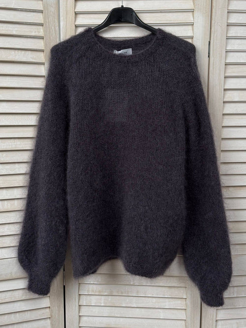 Dark gray sweater on a hanger against a wooden panel background