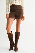 Person wearing brown lace shorts and knee-high brown boots on a white background