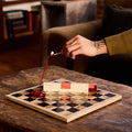 Person lighting a candle on a checkered board with a cozy indoor setting.