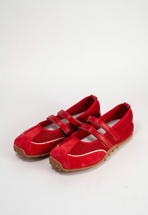 A pair of red Mary Jane style shoes with perforated side panels, double hook-and-loop straps, and tan soles, photographed on a light gray studio background.