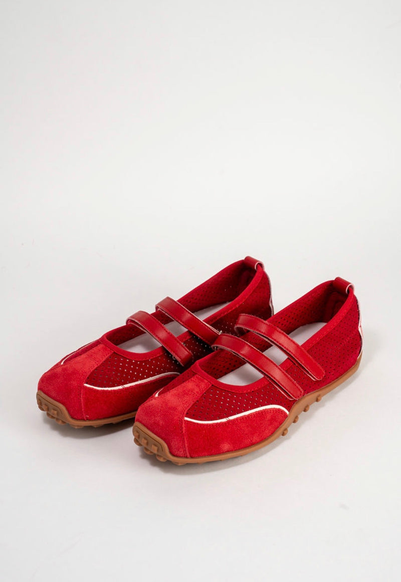 A pair of red Mary Jane style shoes with perforated side panels, double hook-and-loop straps, and tan soles, photographed on a light gray studio background.