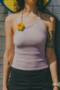 Woman wearing a purple halter top with a floral accessory against a brick wall.