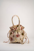 A small drawstring handbag with a soft, mottled beige, cream, and muted red pattern, featuring double top handles, photographed on a seamless light gray studio background.