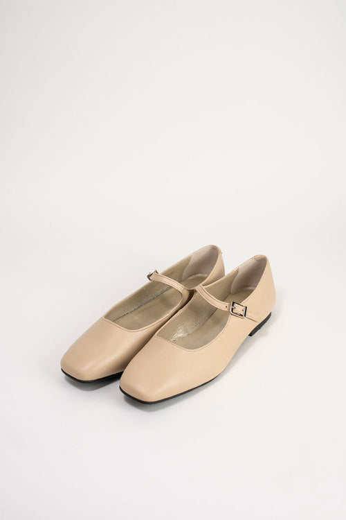 A pair of beige leather Mary Jane flats with square toes and small buckle straps, photographed on a clean white studio background.