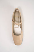 A single beige Mary Jane flat shoe with a square toe and a small silver buckle on the ankle strap, photographed from a top-down angle on a light gray background.