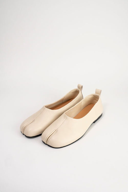 A pair of light beige leather tabi-style flats with a split toe and pull tabs, displayed on a clean white background.