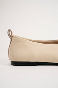 A close-up side view of a beige leather ballet flat shoe with a black sole, set against a plain light gray background.