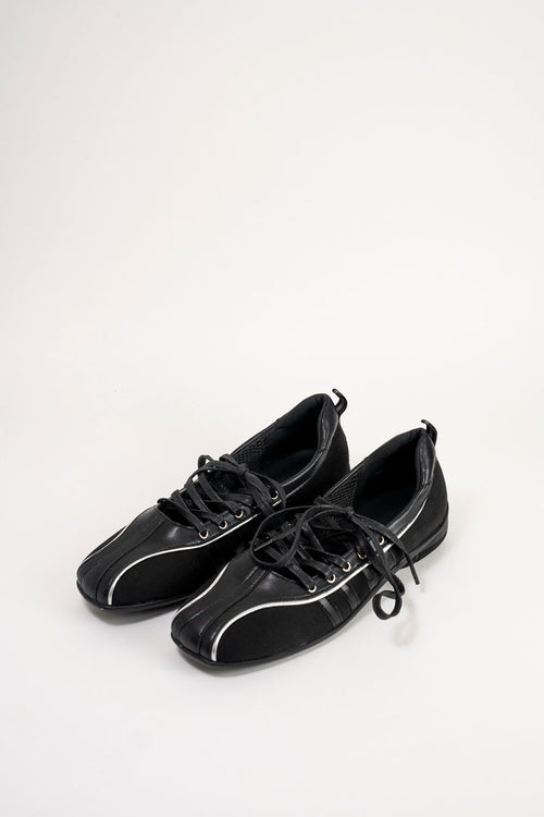 A pair of black leather low-top sneakers with white piping details and black laces, displayed on a clean white background.