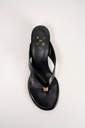 A black leather thong sandal with a low block heel and a small gold metal accent, shown from a top-down view on a light gray background. The insole features the brand logo 'KMB' in gold.
