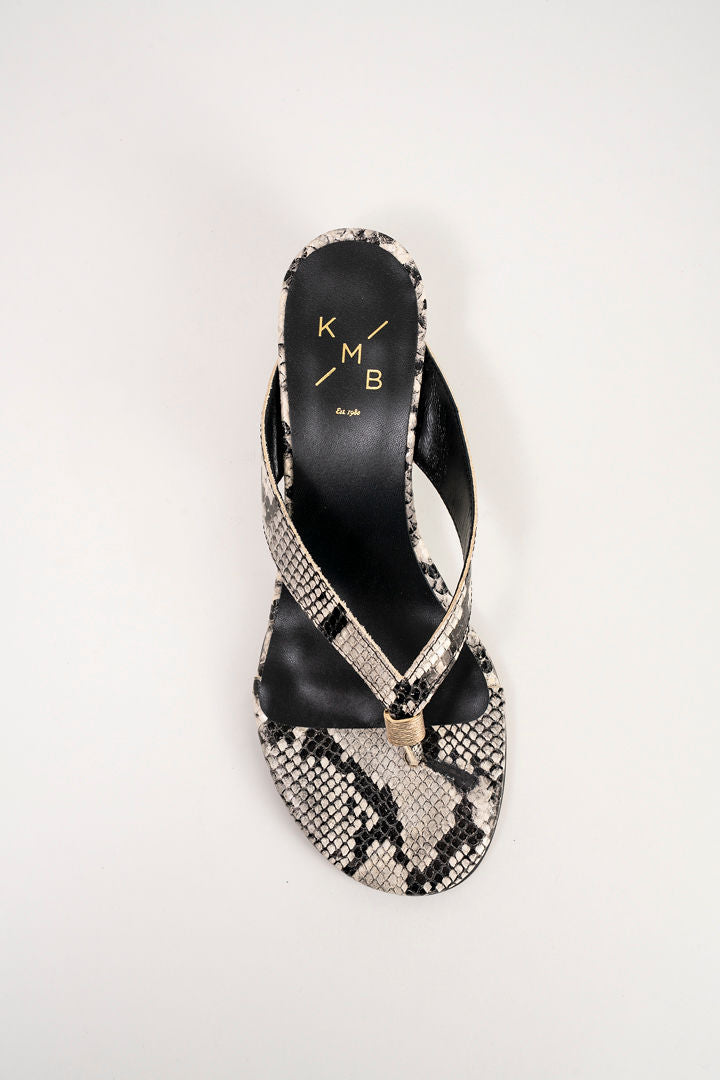 A single women's heeled sandal shown from a top-down view on a light gray background. The sandal features a snakeskin-patterned strap and toe cap with black heel counter and a small gold-tone metal accent at the center.