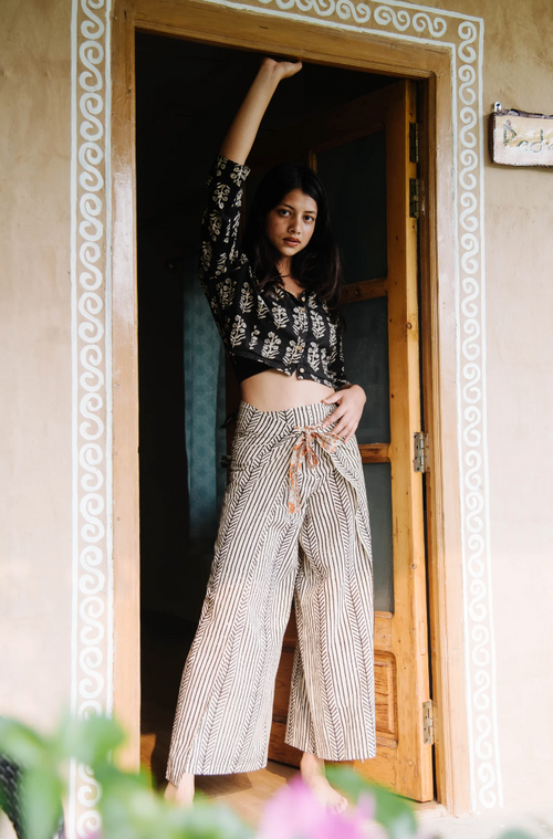 Woman standing in a doorway wearing a patterned top and wide-leg pants.