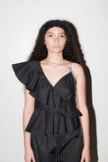 Woman wearing a black ruffled top and pants against a white background