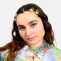Person with floral headband and colorful outfit on a plain background