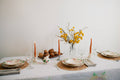Easter table setting with plates, candles, and a vase of yellow flowers on a white tablecloth.