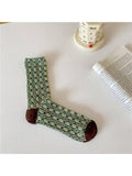 Green floral-patterned sock on a white surface with a book and calendar in the background.