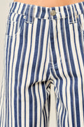 Close-up of a pair of blue and white vertically striped denim pants, showing the waistband, button, belt loops, and front pocket area.