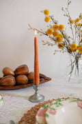 Orange candle in a metal holder on a table with decorative elements.