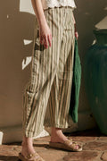 Person wearing striped pants standing next to a large green vase on a stone floor.