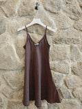 Brown slip dress hanging on a hanger against a stone wall.