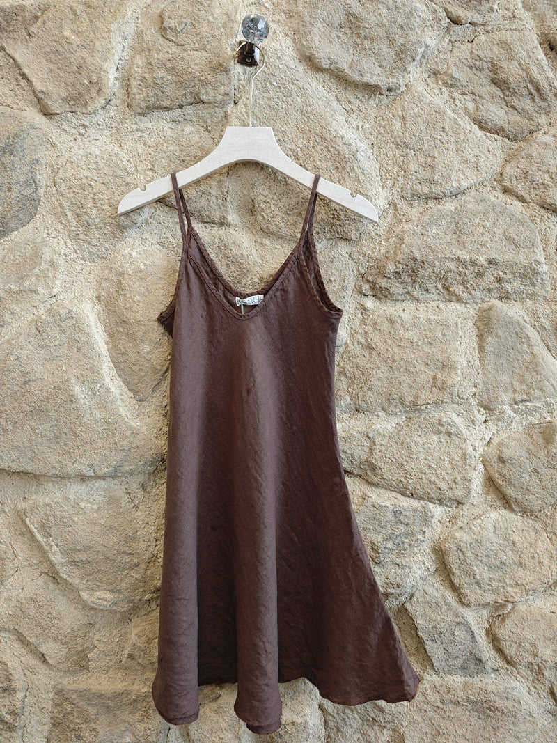 Brown slip dress hanging on a hanger against a stone wall.