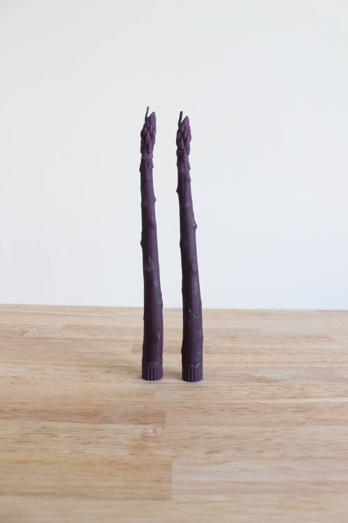Two purple asparagus stalks on a wooden surface with a white background