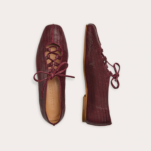 Pair of maroon textured shoes with laces on a light beige background