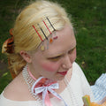 Person with decorative hairpins and makeup, holding a piece of fruit outdoors.