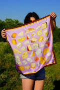 Person holding a purple scarf with cheese illustrations in an outdoor setting
