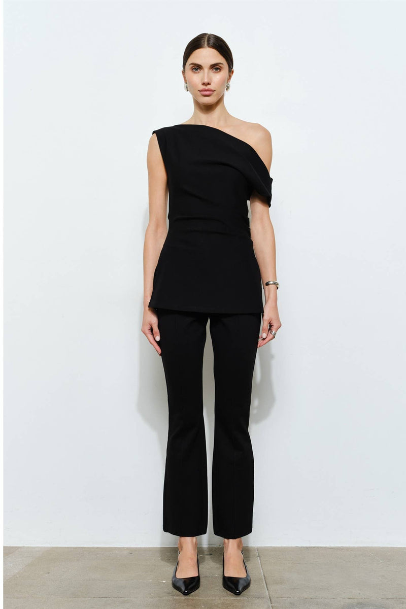 Woman wearing a black one-shoulder top and black pants against a white background