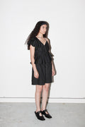 Woman wearing a black dress with ruffled sleeves against a white background