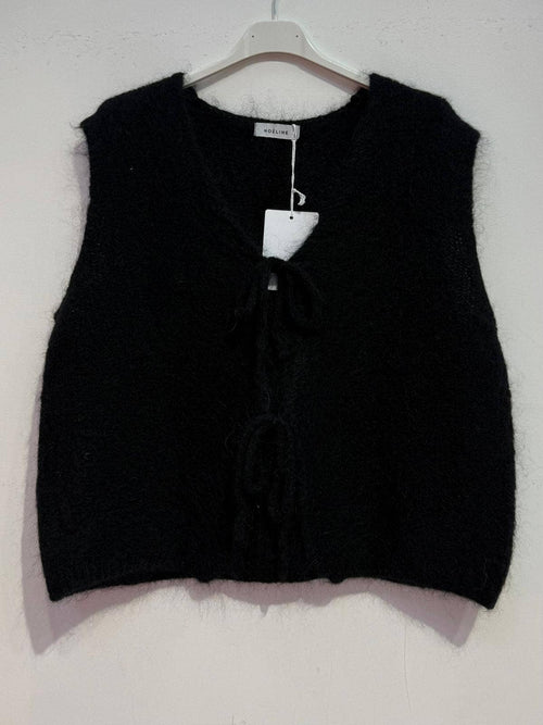Black knitted vest on a hanger against a white background