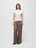 A model stands against a light gray studio background wearing a white mock-neck short-sleeve top and brown pinstriped wide-leg trousers.