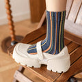 Colorful striped socks worn with white shoes on a wooden chair.