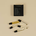 Five small perfume sample vials with black spray caps are arranged on a warm beige background below a black rectangular card labeled 'FOR EXPLORATION' and 'Pola Santo.' The vials contain clear and golden liquids, and several are labeled with scent names such as 'Sakura Odor,' 'Hawaii Scent,' 'Cactus Flower,' 'Desert Kosh,' and 'Pola Santo.