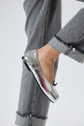 Silver loafers worn with gray jeans on a white background