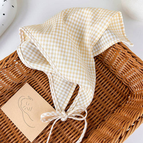 Checkered baby bonnet on a wicker basket with a card