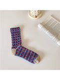 Blue and red patterned sock on a white surface with a book and small container in the background