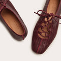 Pair of maroon textured shoes with red laces on a white background