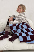 Woman sitting on a couch with a checkered blanket, wearing striped shirt and dark socks.