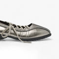 A metallic silver lace-up shoe with a textured finish, gray laces, and a black sole, shown in a side profile on a white background.