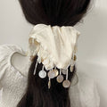 Decorative hair accessory with white fabric and gold coins on a blurred background