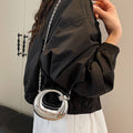 Person wearing a black jacket with a silver circular bag over their shoulder.