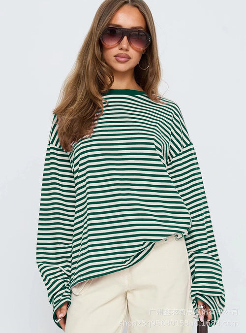 Woman wearing a green and white striped shirt with sunglasses on a plain background